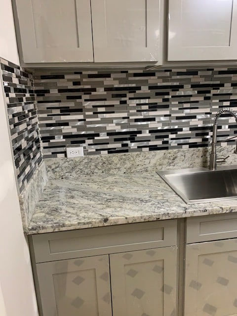 Quarts countertop with gray and black backsplash with stainless steel sink