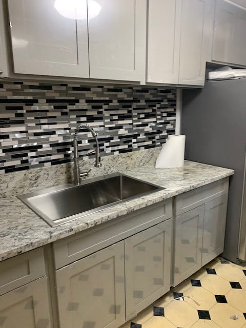 Quarts countertop with gray and black backsplash with stainless steel sink and gray cabinets